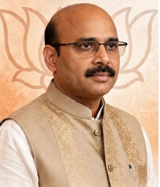 Formal portrait of Harish Dwivedi in a beige jacket against a patterned background
