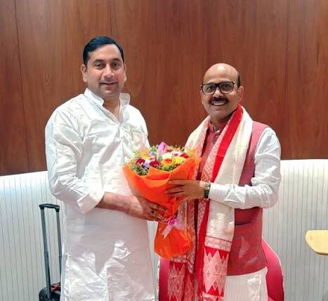 Harish Dwivedi receiving a welcome bouquet at a meeting, wearing a traditional gamosa