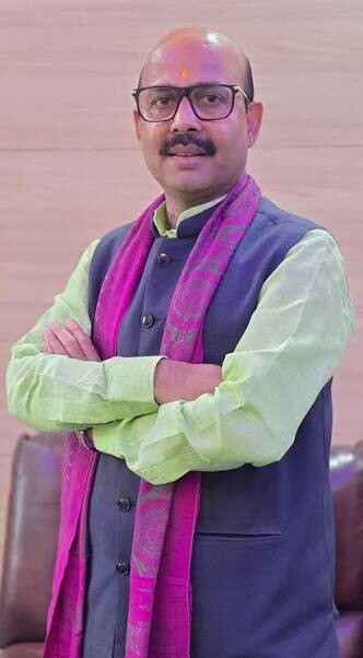 Harish Dwivedi standing indoors wearing a magenta stole over a dark jacket