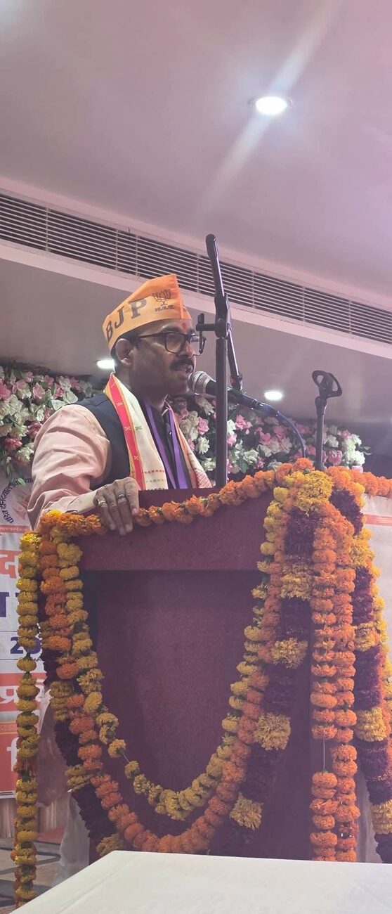 Harish Dwivedi addressing an audience from a podium decorated with marigold garlands